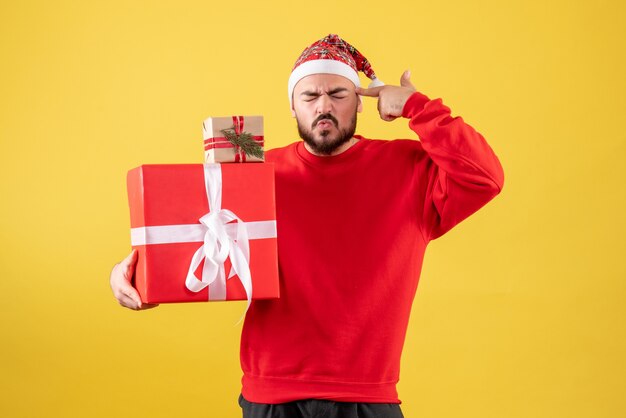 Vorderansicht junger Mann, der Weihnachtsgeschenke auf einem gelben Hintergrund hält