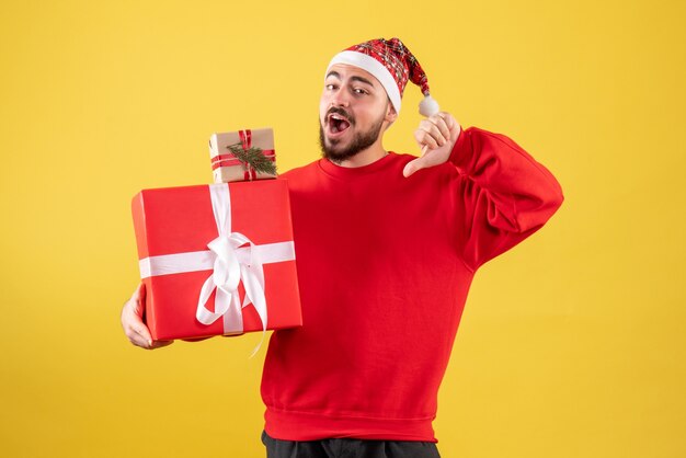 Vorderansicht junger Mann, der Weihnachtsgeschenke auf einem gelben Hintergrund hält