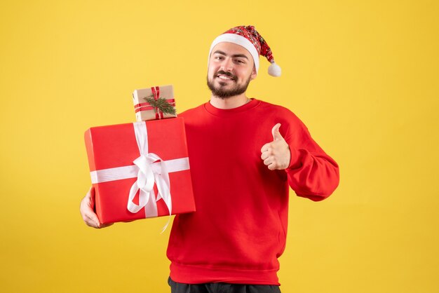 Vorderansicht junger Mann, der Weihnachtsgeschenke auf einem gelben Hintergrund hält