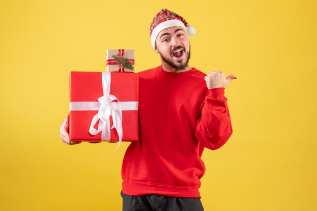 Vorderansicht junger Mann, der Weihnachtsgeschenke auf einem gelben Hintergrund hält