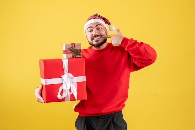 Vorderansicht junger Mann, der Weihnachtsgeschenke auf einem gelben Hintergrund hält