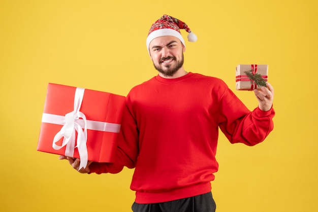 Kostenloses Foto vorderansicht junger mann, der weihnachtsgeschenke auf einem gelben hintergrund hält