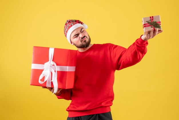 Vorderansicht junger Mann, der Weihnachtsgeschenke auf einem gelben Hintergrund hält