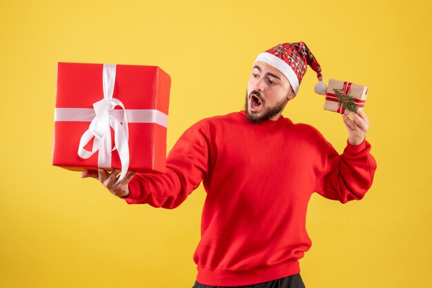 Vorderansicht junger Mann, der Weihnachtsgeschenke auf einem gelben Hintergrund hält