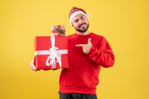 Vorderansicht junger Mann, der Weihnachtsgeschenke auf einem gelben Hintergrund hält