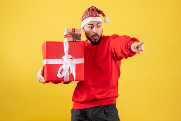 Vorderansicht junger Mann, der Weihnachtsgeschenke auf einem gelben Hintergrund hält