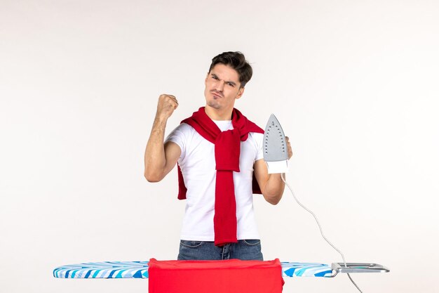 Vorderansicht junger Mann hinter Bügelbrett mit Bügeleisen auf weißem Hintergrund Hausarbeit Emotion Wäscherei Mann nach Hause sauber wütend