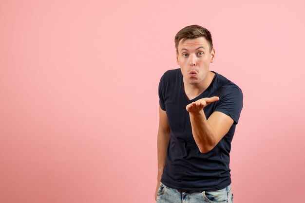 Vorderansicht junger Mann im blauen T-Shirt, das Luftküsse auf rosa Hintergrundemotionsfarbmodell menschliches Männchen sendet