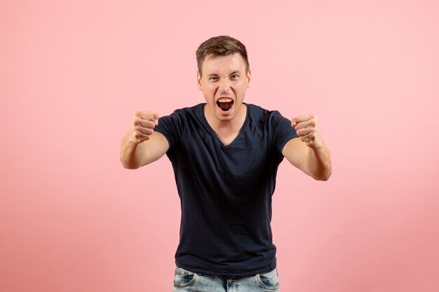 Vorderansicht junger Mann im blauen T-Shirt, das sich emotional auf männlichem Emotionsfarbmodellmensch des rosa Hintergrunds emotional freut