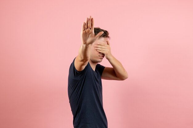 Vorderansicht junger Mann im dunkelblauen Hemd, das sein Gesicht auf rosa Hintergrund männlicher menschlicher Farbmannmodellemotion bedeckt