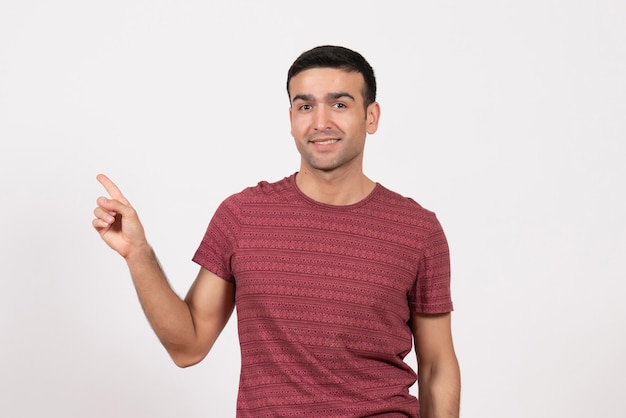 Vorderansicht junger Mann im dunkelroten T-Shirt lächelt und posiert auf weißem Hintergrund