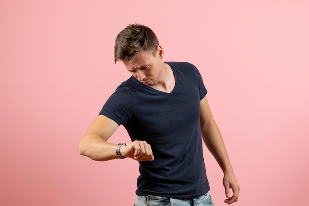 Vorderansicht junger Mann im dunklen T-Shirt, der die Zeit auf rosafarbenem Hintergrund überprüft