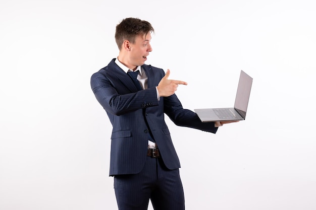 Vorderansicht junger Mann im eleganten klassischen Anzug mit Laptop auf weißem Hintergrund