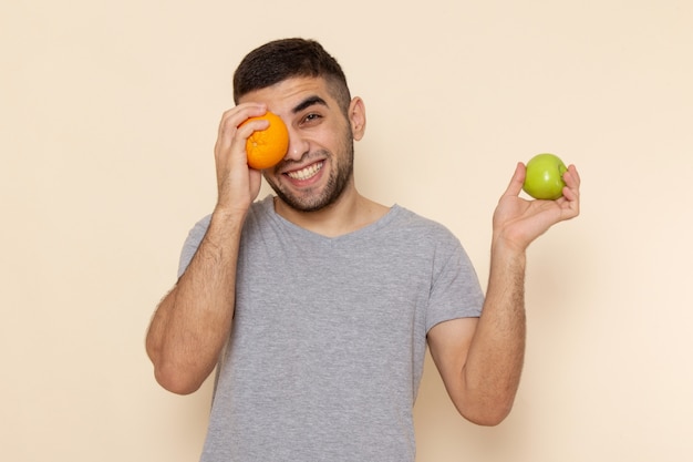 Vorderansicht junger Mann im grauen T-Shirt, das Apfel und orange Schreibtisch hält