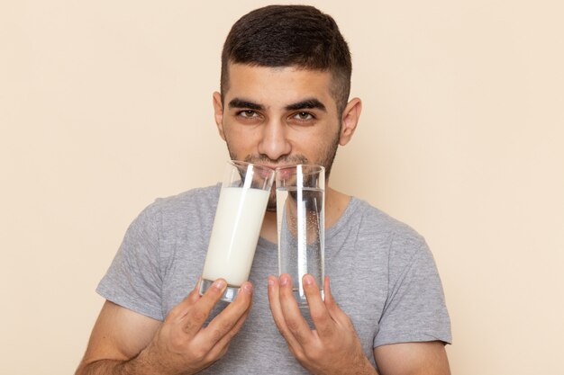 Vorderansicht junger Mann im grauen T-Shirt, das Gläser der Wassermilch auf Beige hält