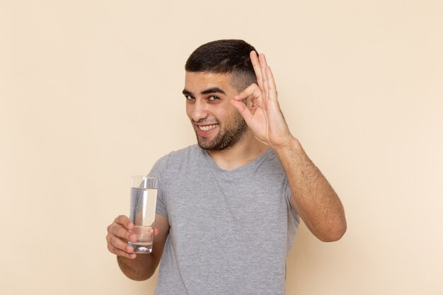 Vorderansicht junger Mann im grauen T-Shirt, das Glas Wasser hält