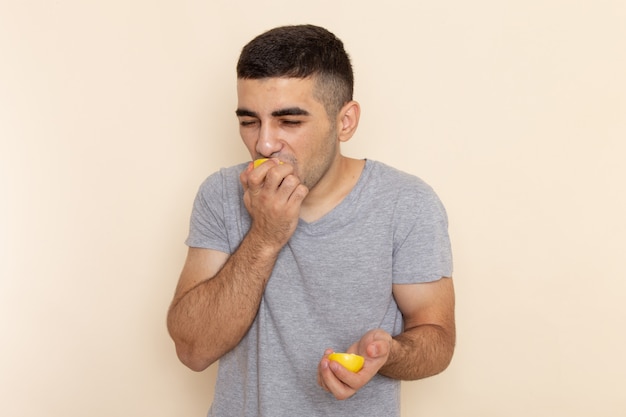 Kostenloses Foto vorderansicht junger mann im grauen t-shirt, das zitrone auf beige isst