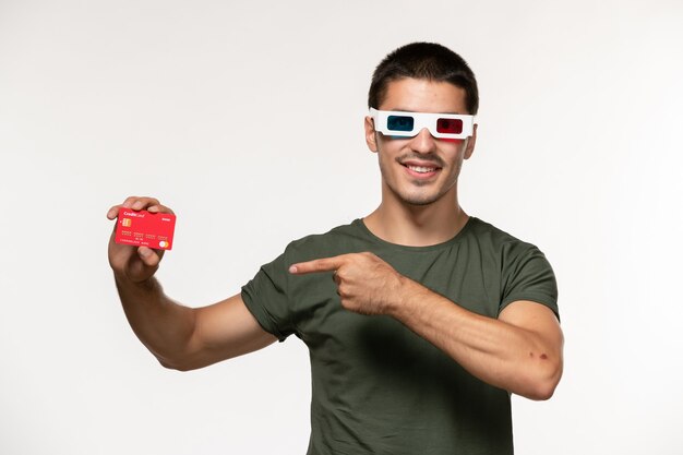 Vorderansicht junger Mann im grünen T-Shirt, das Bankkarte in d Sonnenbrille auf weißen Wandfilm einsamen Kinofilmen hält