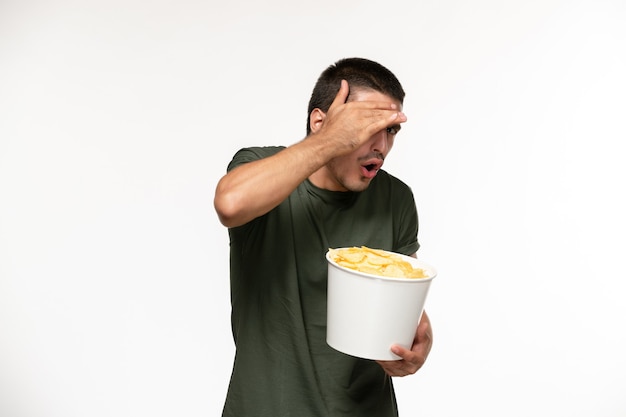 Vorderansicht junger mann im grünen t-shirt, das kartoffel-cips hält, die film auf dem einsamen filmfilmkino der weißen wandperson ansehen