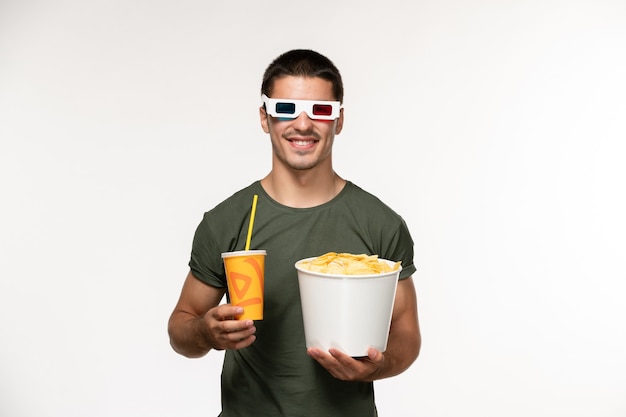 Vorderansicht junger mann im grünen t-shirt, das kartoffelspitzen-soda in -d sonnenbrille auf weißen wandfilm-männlichen einsamen filmen hält