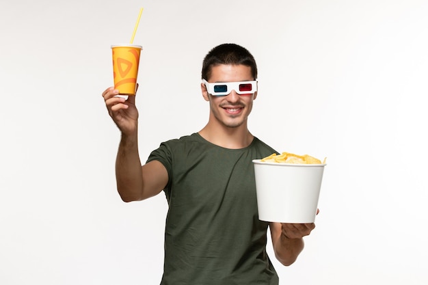 Vorderansicht junger Mann im grünen T-Shirt, das Kartoffelspitzen-Soda in der d Sonnenbrille auf dem weißen Wandfilm des männlichen einsamen Filmkinos der weißen Wand hält