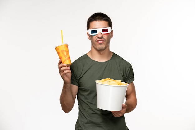 Vorderansicht junger Mann im grünen T-Shirt, das Kartoffelspitzen-Soda in der d Sonnenbrille auf dem weißen Wandfilm des männlichen einsamen Filmkinos der weißen Wand hält
