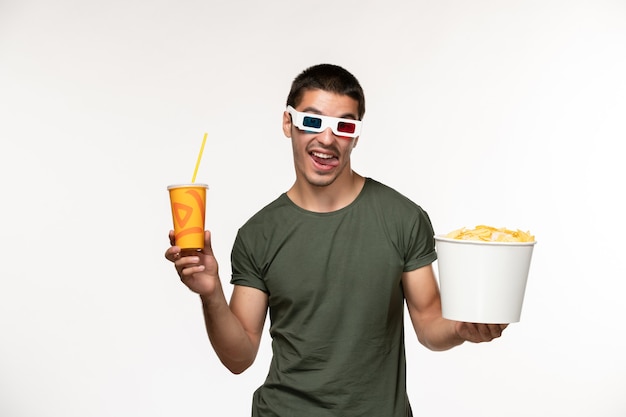 Vorderansicht junger Mann im grünen T-Shirt, das Kartoffelspitzen-Soda in der d Sonnenbrille auf dem weißen Wandfilm-männlichen einsamen Filmkino hält