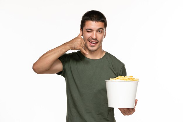 Vorderansicht junger Mann im grünen T-Shirt, das Korb mit Kartoffelspitzen auf weißem Wand-Filmkino des einsamen Vergnügens hält