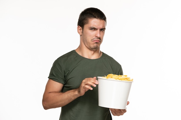 Vorderansicht junger Mann im grünen T-Shirt, das Korb mit Kartoffelspitzen hält und sie auf weißem Wand-Filmkino des einsamen Genusses isst