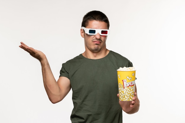 Vorderansicht junger Mann im grünen T-Shirt, das Popcorn in d Sonnenbrille hält Film auf weißen Wandfilm einsamen Kinofilmen sieht