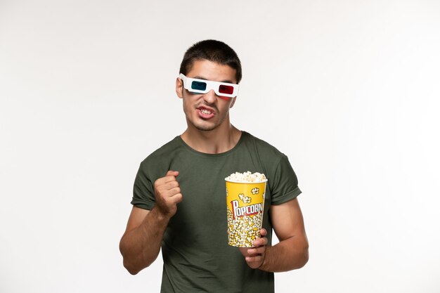 Vorderansicht junger Mann im grünen T-Shirt, das Popcorn-Paket in d Sonnenbrille auf weißem Wandfilm einsamen Kino-Männerfilm hält