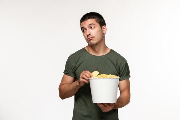 Vorderansicht junger Mann im grünen T-Shirt mit Kartoffel-Cips, die Film auf hellweißem Wandfilm sehen Person männlich einsames Filmkino