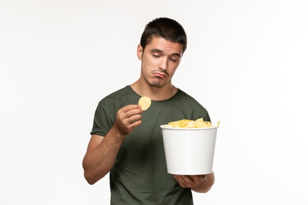 Vorderansicht junger Mann im grünen T-Shirt mit Kartoffelspitzen und Essen auf dem einsamen Filmfilmkino der weißen Wandperson