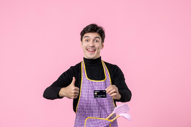 Vorderansicht junger Mann im Umhang mit schwarzer Bankkarte auf rosa Hintergrund Job Beruf Koch Chef Uniform Küche Farbe Geld horizontal