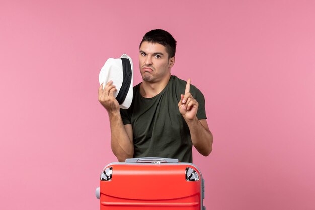 Vorderansicht junger Mann im Urlaub, der seinen Hut auf dem rosa Raum hält