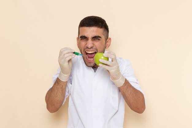 Vorderansicht junger Mann im weißen Anzug, der Handschuhe trägt, die Apfel injizieren, der auf Beige schreit