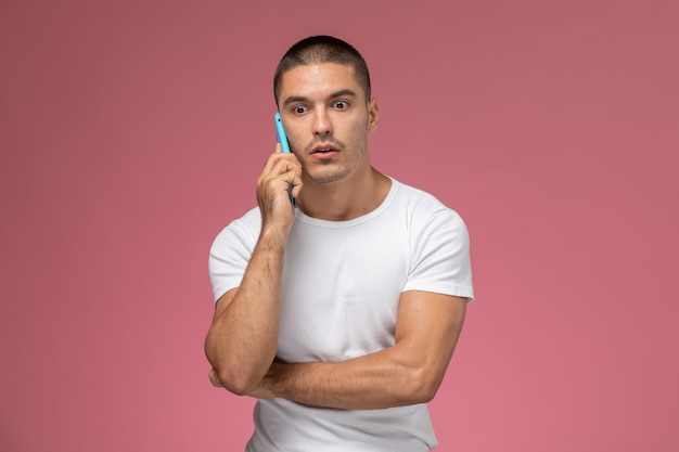 Vorderansicht junger Mann im weißen Hemd, das am Telefon mit gestörtem Ausdruck auf rosa Hintergrund spricht