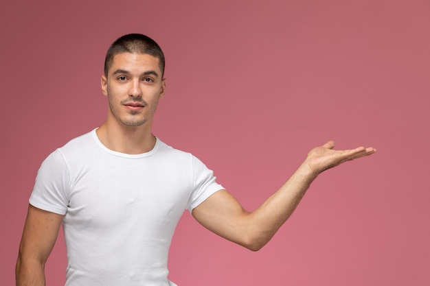 Vorderansicht junger Mann im weißen Hemd, das mit seiner Hand auf rosa Hintergrund aufwirft