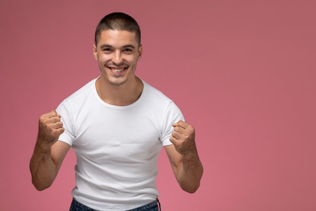 Vorderansicht junger Mann im weißen Hemd, das sich mit Lächeln auf dem rosa Hintergrund freut