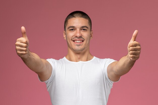 Vorderansicht junger Mann im weißen Hemd, das wie Zeichen zeigt, die auf rosa Hintergrund lächeln