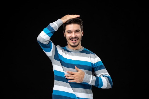 Vorderansicht junger Mann in blau gestreiftem Trikot auf der schwarzen Wand Foto Farbe Emotion Dunkelheit menschliches Modell