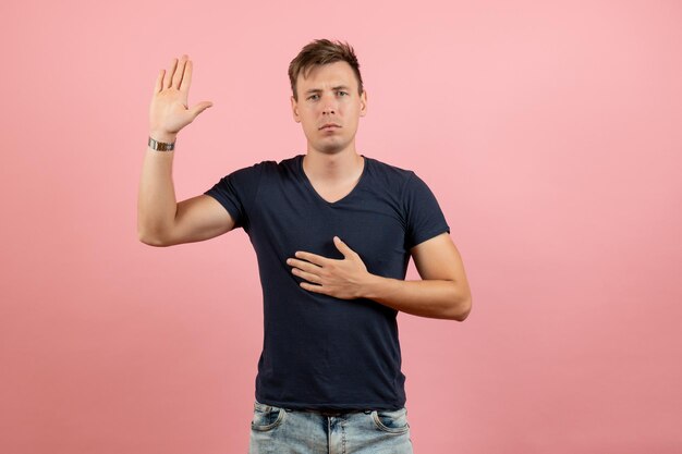 Vorderansicht junger Mann in dunklem T-Shirt und Jeans, die seine Hand auf rosa Hintergrund zeigen
