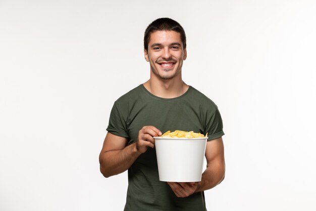 Vorderansicht junger Mann in grünem T-Shirt mit Kartoffel-Cips, die Film ansehen und auf weißem Filmfilmmann des einsamen Filmkinos der weißen Wandfilmperson lächeln