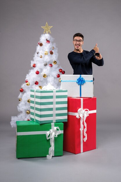 Vorderansicht junger Mann mit Bankkarte auf grauem Boden Neujahrsgeschenk Weihnachten