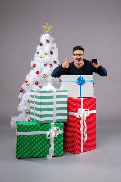 Vorderansicht junger Mann mit Bankkarte auf grauem Schreibtisch Neujahrsgeschenk Weihnachten