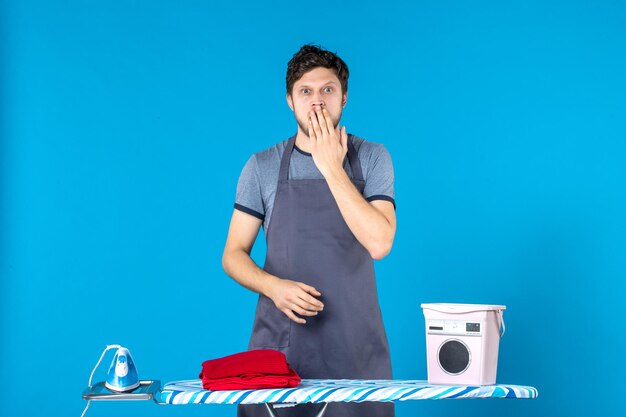 Vorderansicht junger Mann mit Bügelbrett auf blauem Hintergrund Hausarbeit Bügeleisen Wäschereinigung Waschmaschine Mann Farbe