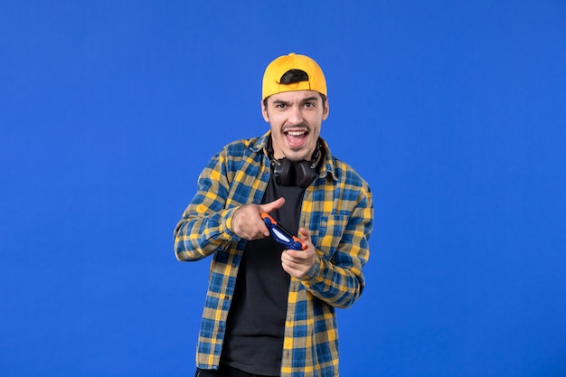 Kostenloses Foto vorderansicht junger mann mit gamepad und kopfhörern, die videospiele auf blauer wand spielen