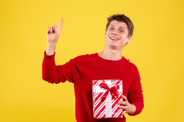 Vorderansicht junger Mann mit Geschenk auf gelbem Hintergrund