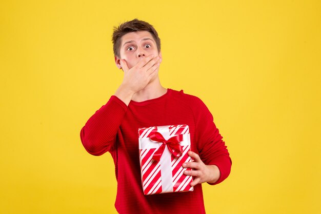 Vorderansicht junger Mann mit Geschenk überrascht auf gelbem Hintergrund