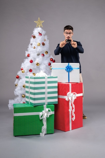 Vorderansicht junger Mann mit Geschenken und Bankkarte auf grauem Boden Urlaub Neujahr Weihnachten